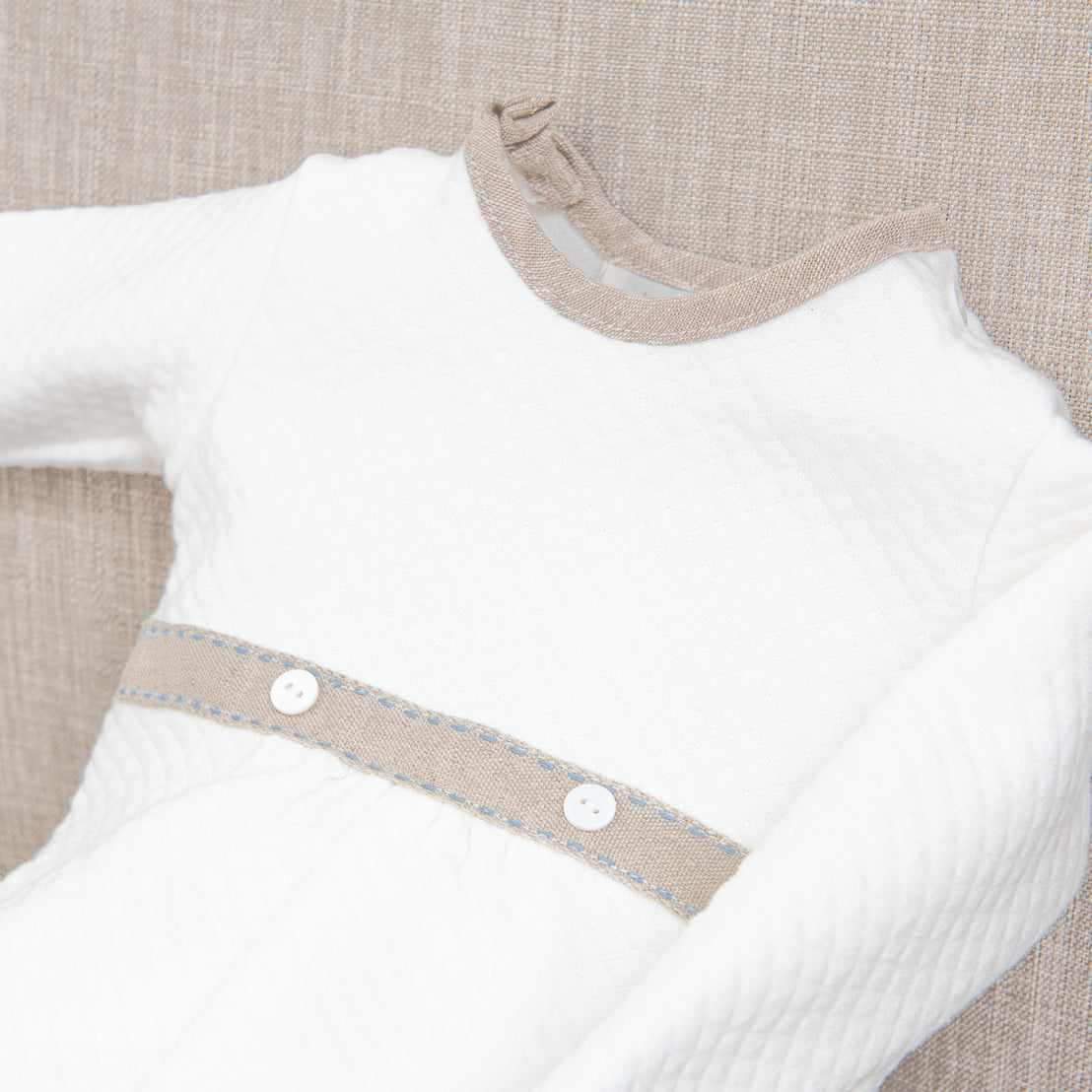 Close-up of a boutique white Austin Romper with an heirloom burlap belt and button details, displayed on a neutral fabric background.