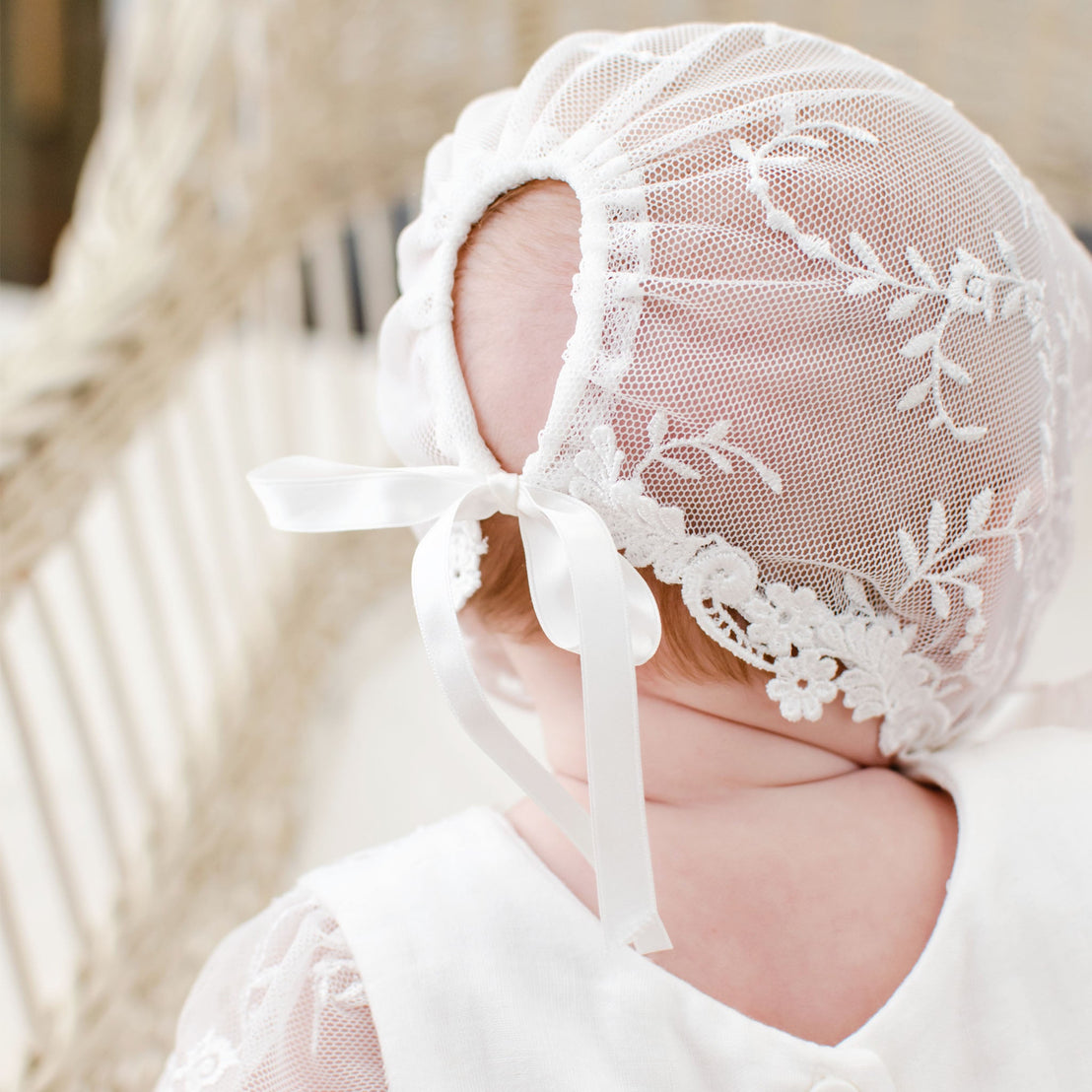A close-up image of a baby wearing an Isla Lace Bonnet, showcasing traditional intricate floral embroidery and tied with a soft ribbon.