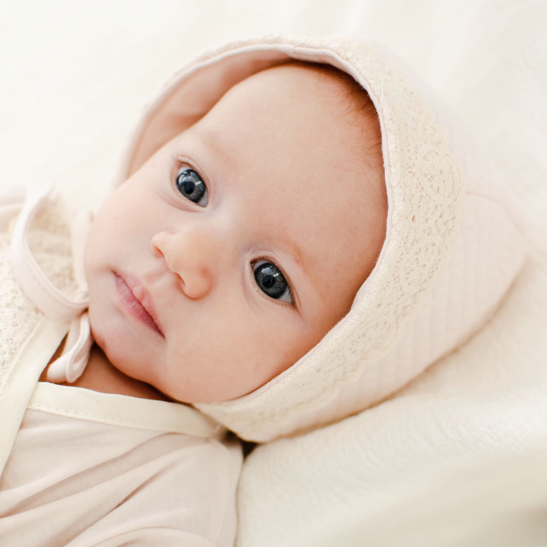 A close-up of a baby with blue eyes wearing the Evelyn Quilt Bonnet looks off camera with a subtle expression.