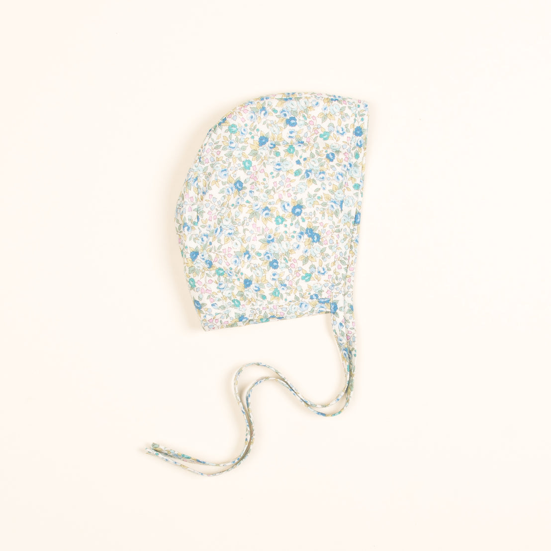 An upscale, handcrafted Petite Fleur Bonnet with a light background, featuring small blue, green, and yellow flowers. The bonnet has a long string tie at the bottom.