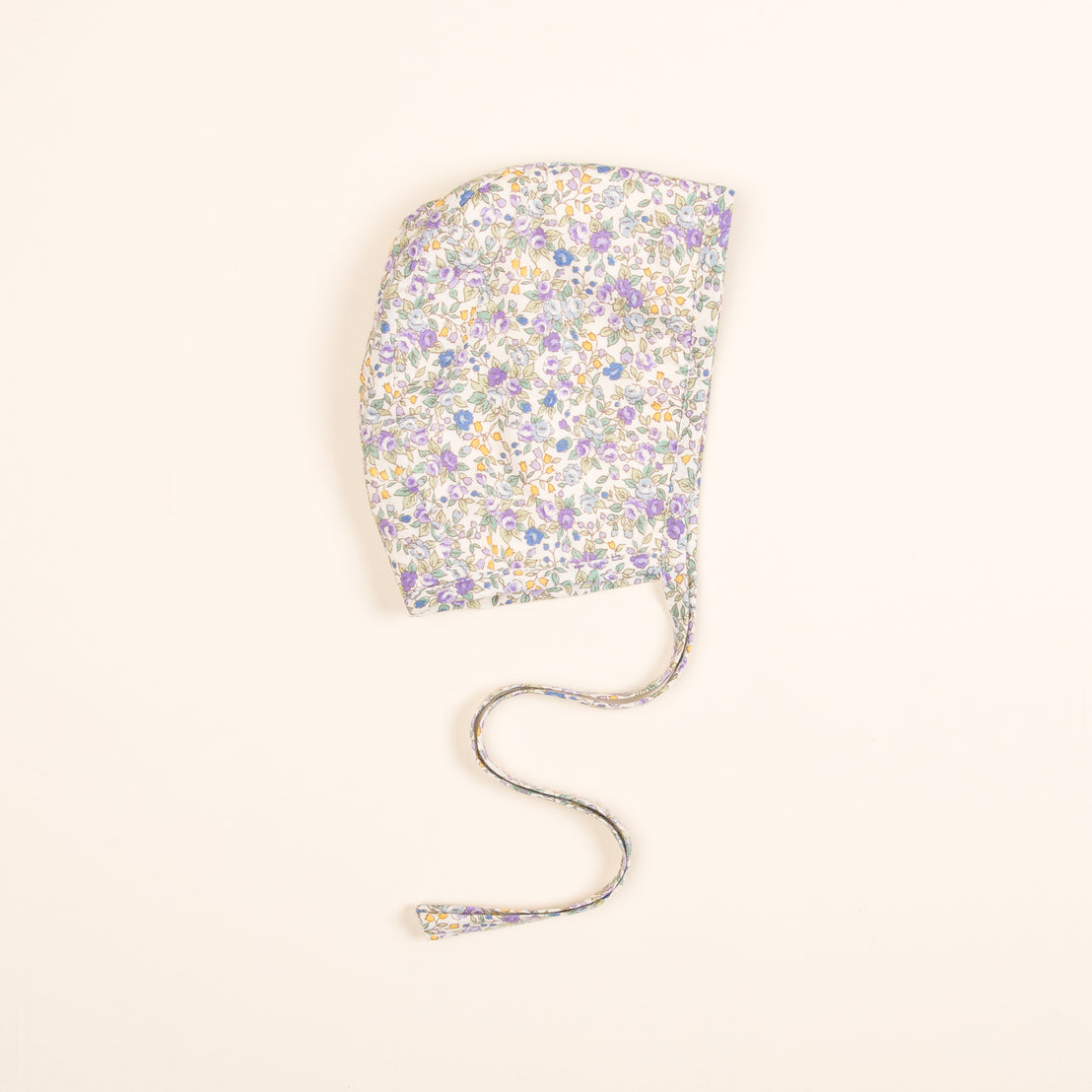 A Petite Fleur Bonnet, floral print fabric shower cap with an extended string, laid flat on a light beige background.