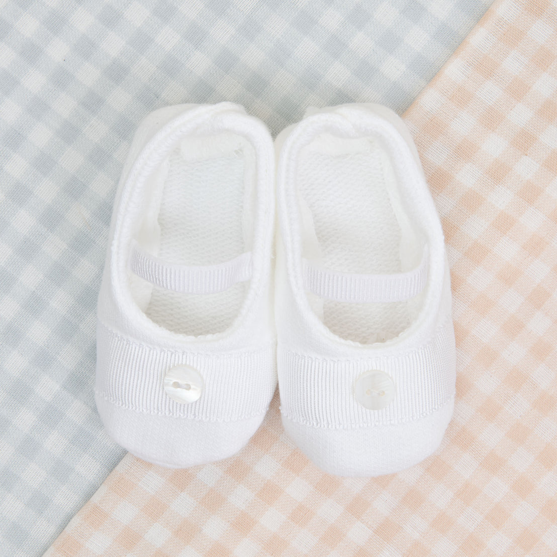 A pair of Ian Booties with buttons on a traditional pastel pink and blue checkered fabric background.