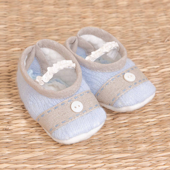 A pair of upscale light blue Austin Booties, displayed on a textured straw background, perfect for coming home. The shoes feature a strap with a button.