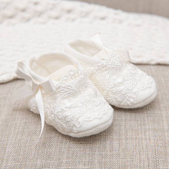 A pair of Madeline Quilted Booties with ribbon ties on a beige fabric background.