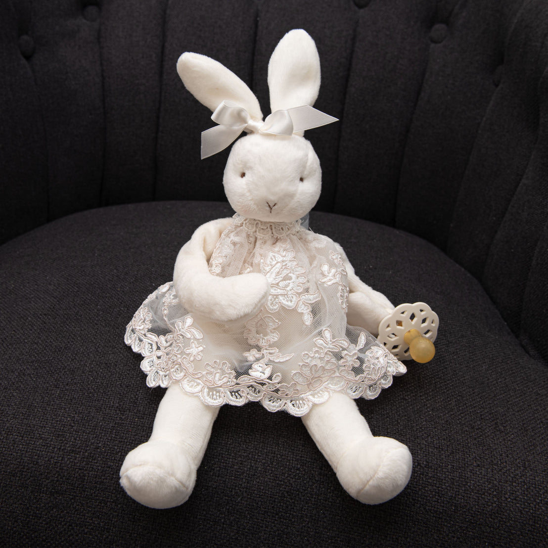 Baby plush bunny toy product photo - wearing a lace christening dress and holding a baby pacifier.