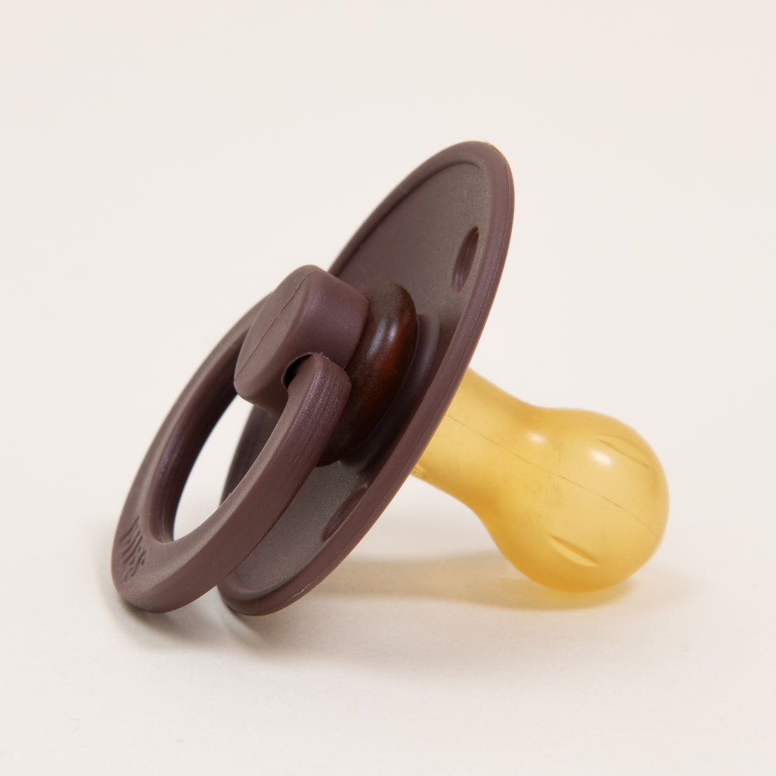 A close-up image of a Bibs Pacifier in Chestnut with a brown handle and a beige rubber nipple on a white background.