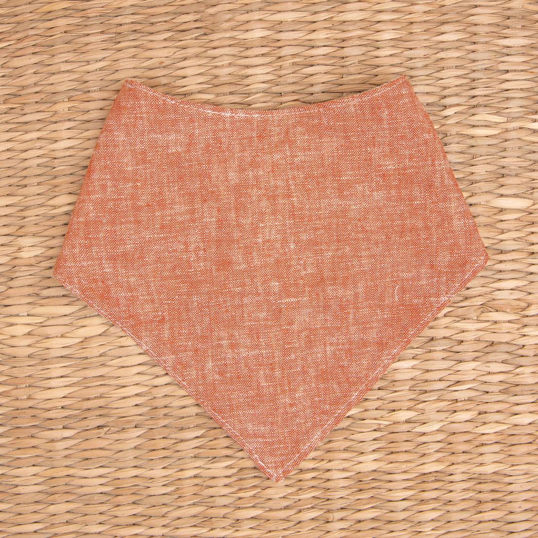 Flat lay photo of the clay colored Silas Bandana Bib in a woven basket