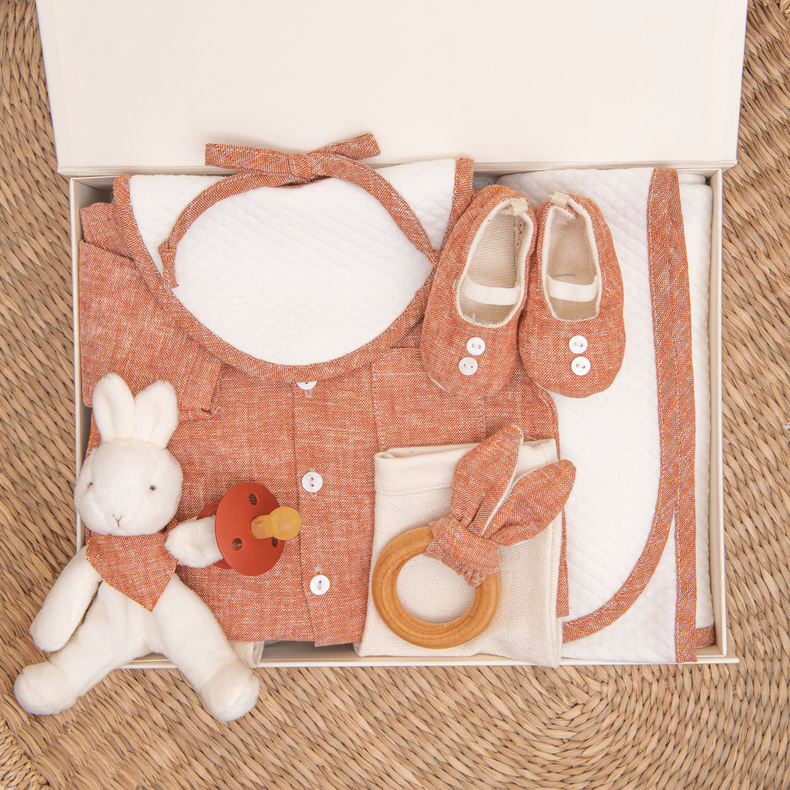 Photo of the clay colored Silas Gift Set in a Gift Box. Included in the box is the shirt, pants, booties, bib, teether, bunny, pacifier, and personalized blanket.