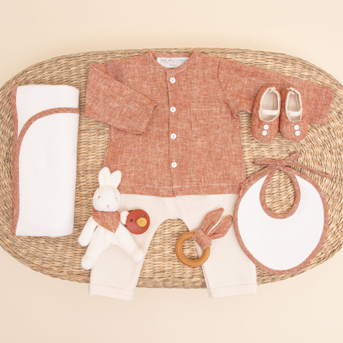 Flat lay photo of the clay colored Silas Gift Set. Included in the photo is the shirt, pants, booties, bib, teether, bunny, pacifier, and personalized blanket.