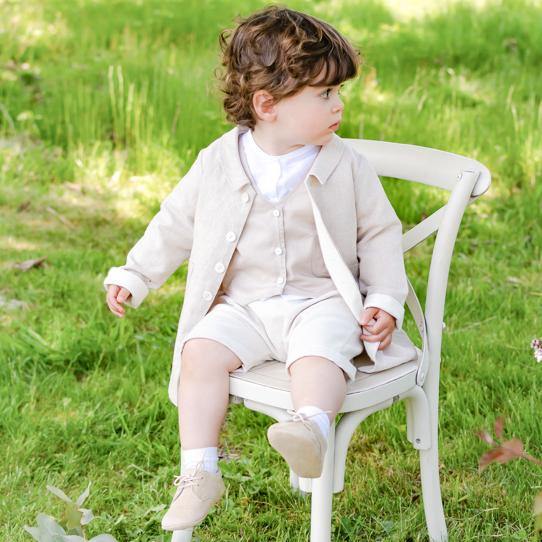 Photo of a baby boy sitting on a chair wearing the Silas Vest Suit underneath the matching Silas Trench Coat