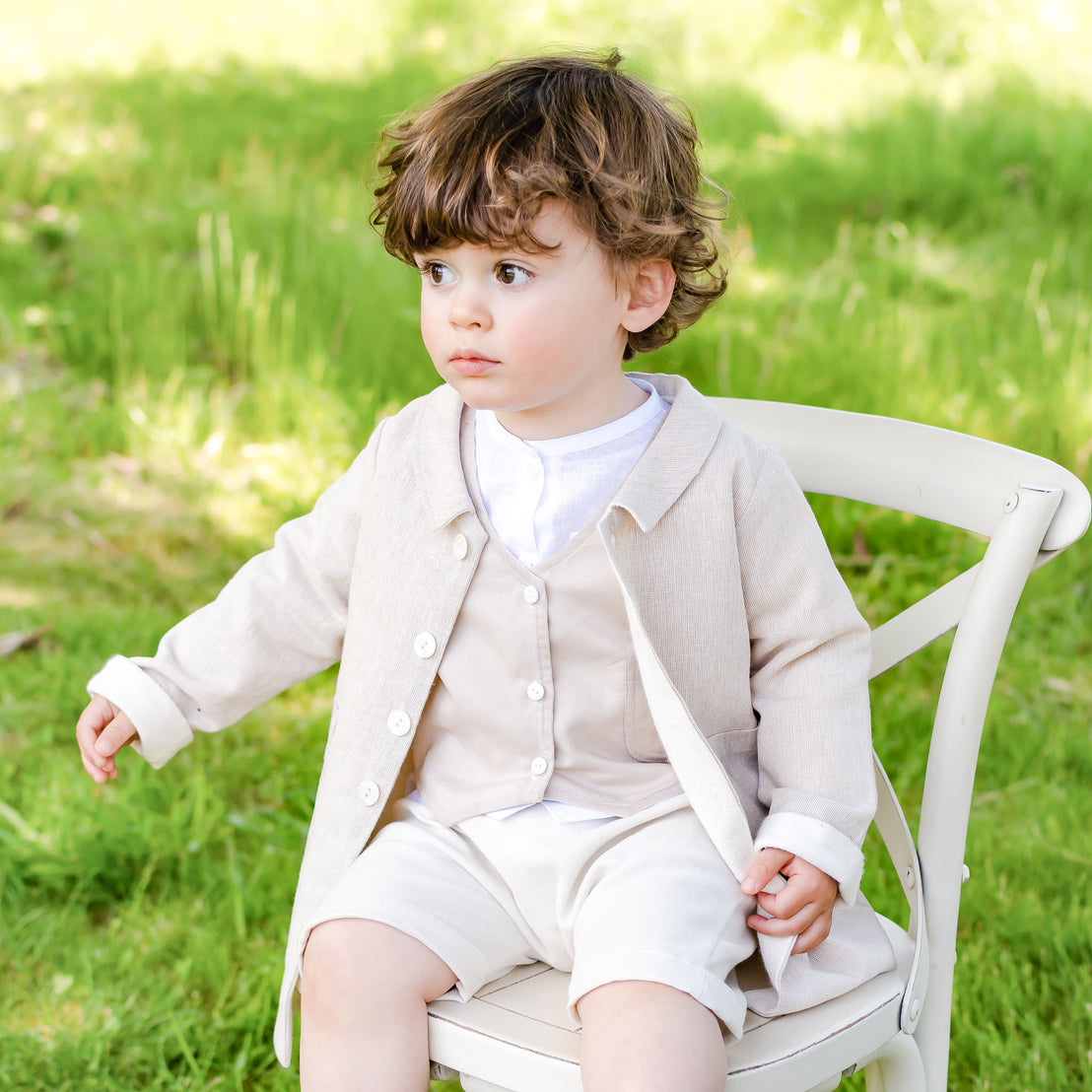 Baby boy sitting on a chair outside and wearing the tan Silas Trench Coat