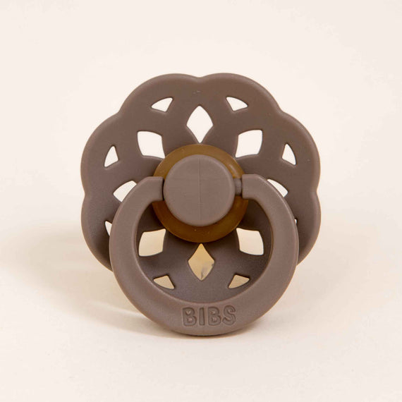 A Bibs Lace pacifier 2 pack in Dark Oak, with a circular scalloped shield and a button-style pull ring, designed and manufactured in Denmark, displayed against a plain light background.