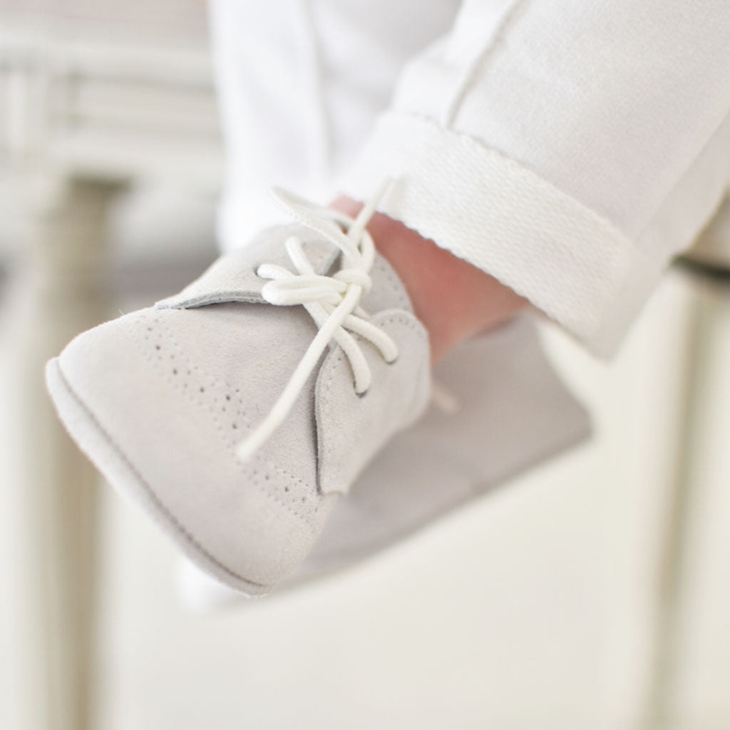 Alternate side photo of a baby wearing the Dove Grey Suede Shoes crafted with a super soft, dove grey suede with detailed edging