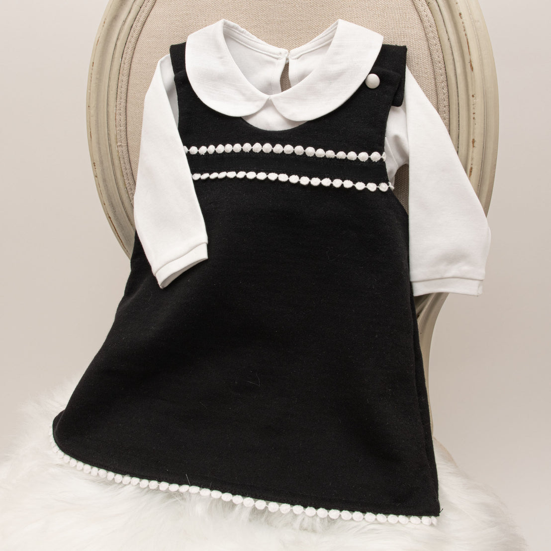 A June Jumper Dress Set with white collar and decorative white pearls displayed on a vintage beige chair with white furry material underneath.