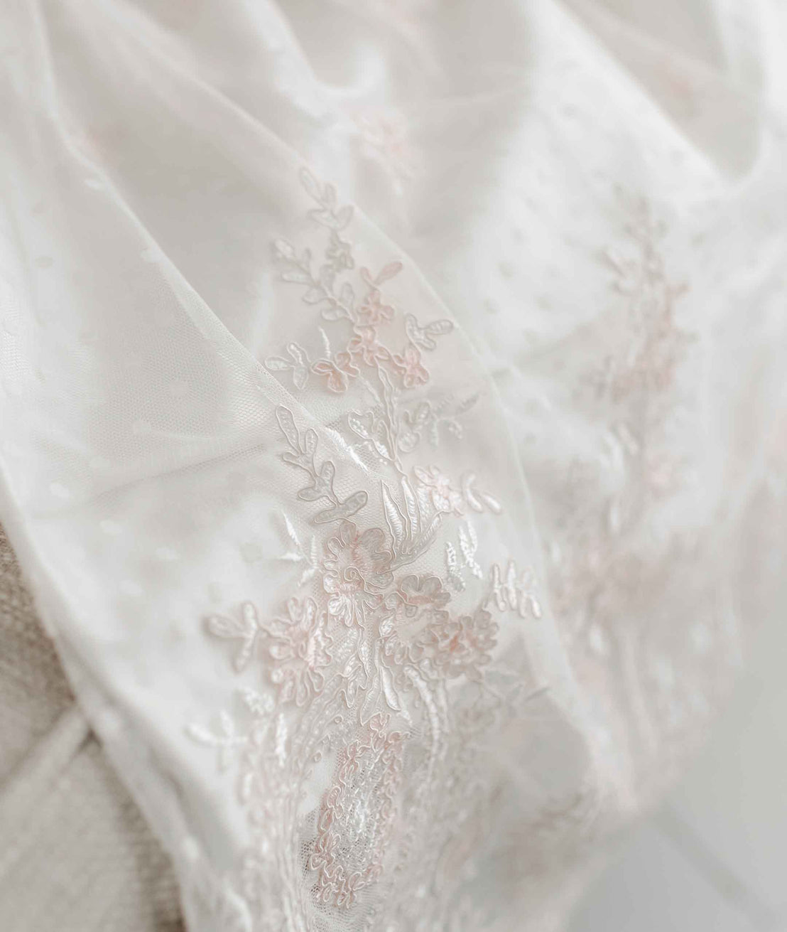 Close-up of the delicate white silk from the Elizabeth Christening Gown's skirt. The skirt features intricate floral embroidery and beadwork, conveying an elegant and textured appearance.