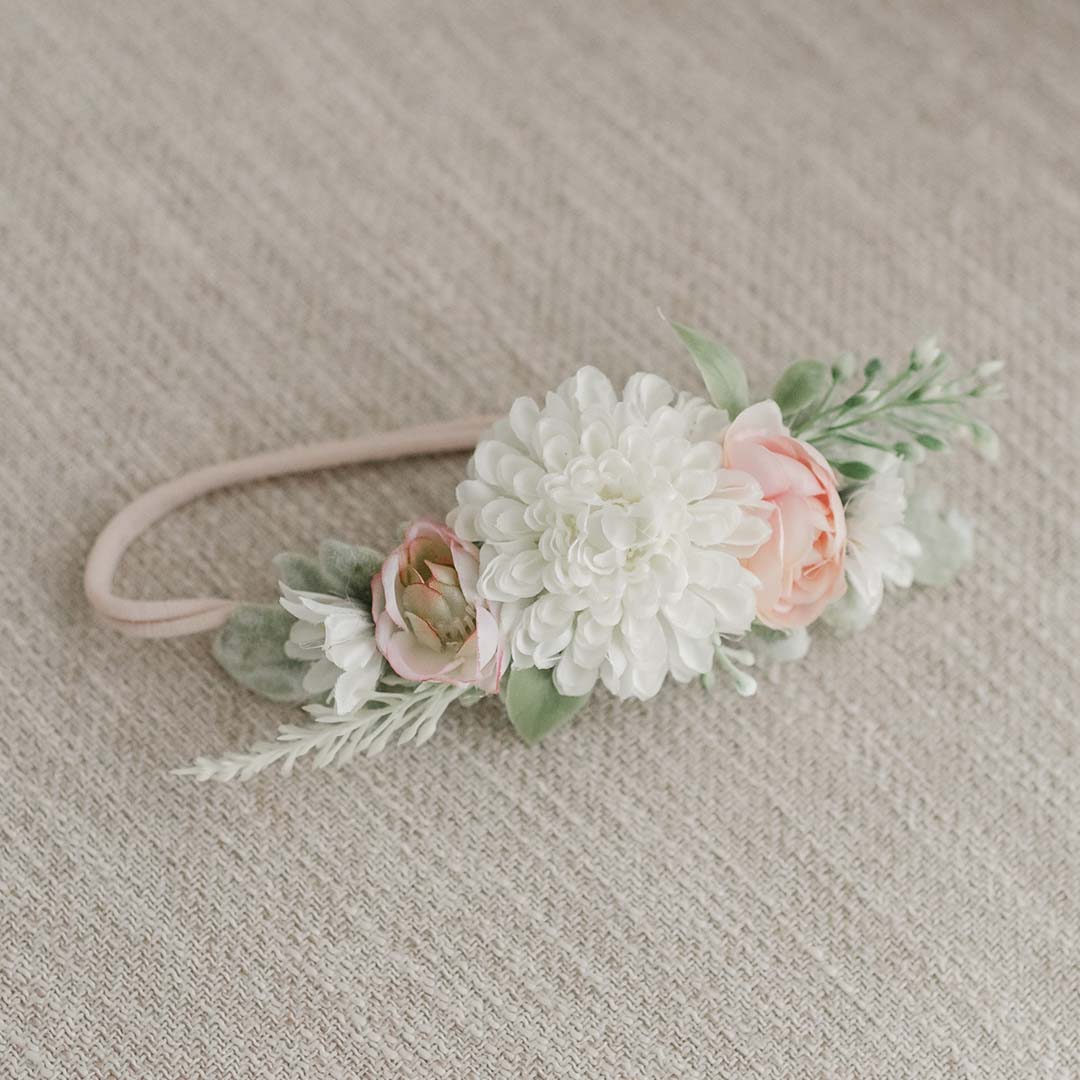 A vintage Elizabeth Flower Headband featuring a large white chrysanthemum, smaller pink roses, and green foliage, set against a neutral textured background.