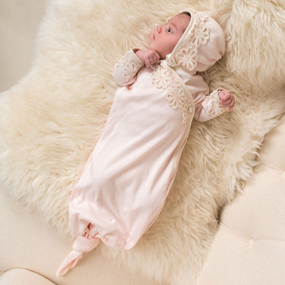 A newborn baby in a Hannah Knot Gown & Bonnet from Baby Beau & Belle lies on a fluffy white fur blanket, looking curiously with wide eyes.