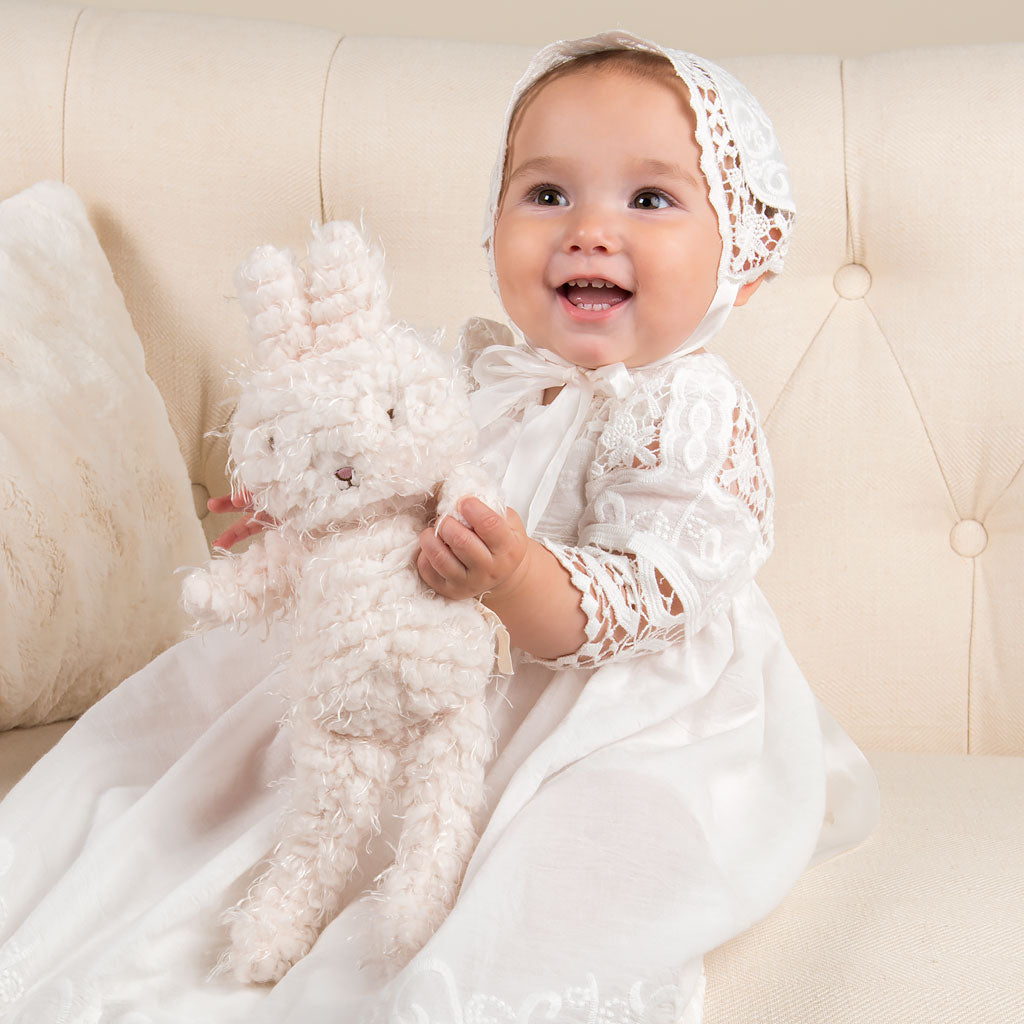 Baby girl smiling and holding a bunny doll and wearing the Adeline baptism gown. 