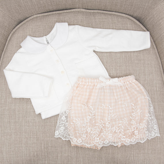 A newborn's Isla French Terry Jacket and upscale peach-colored shorts with lace embroidery are displayed neatly on a gray textured circular chair.