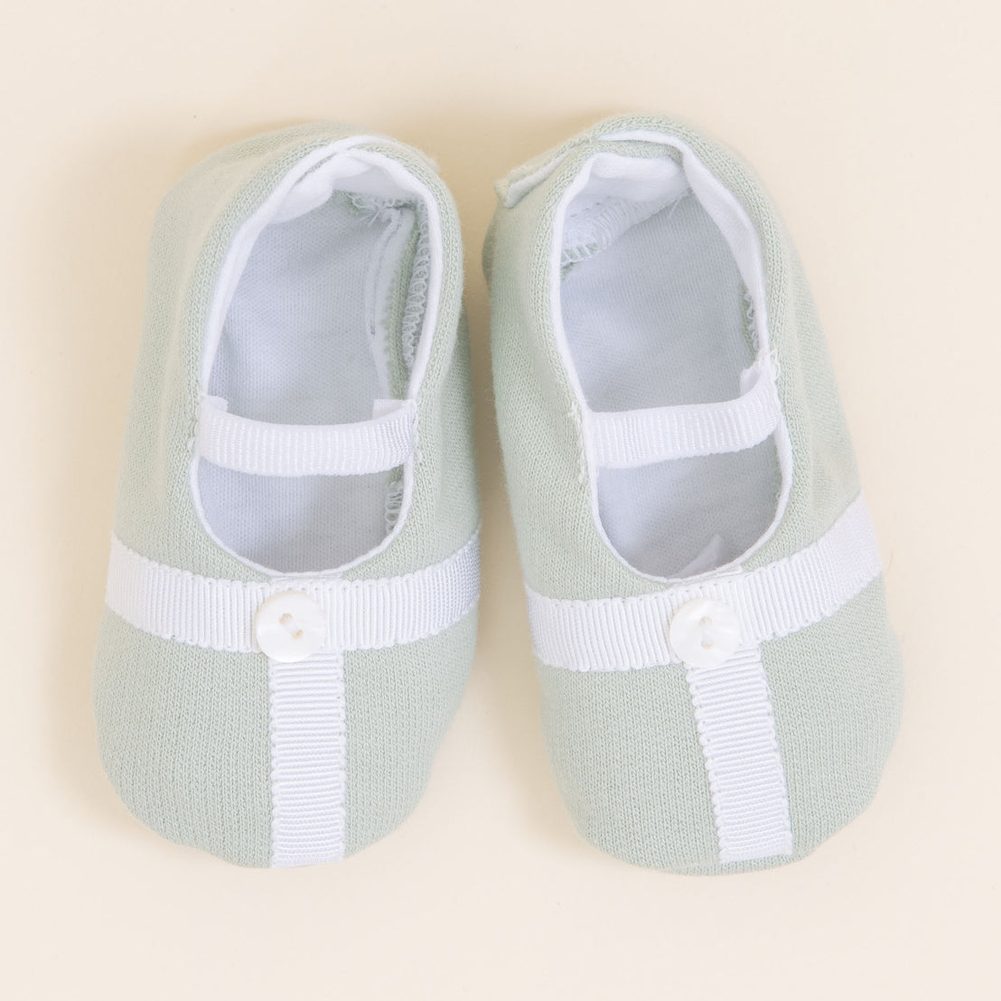 Flat lay photo showing the top detail of the Theodore Booties in green. The booties are made from a 100% French Terry Cotton with a Grosgrain Trim (with button detail) and soft elastic strap.