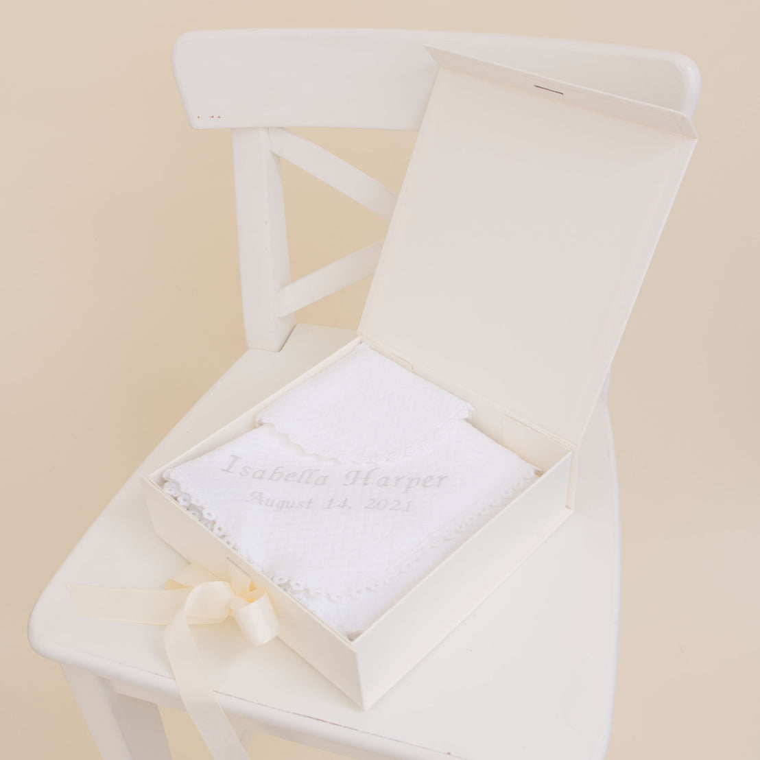 A Baby Beau & Belle Baby Girl Personalized Gift Set on a white chair, personalized with the name "Isabella Harper" and the date "August 14, 2021," decorated with a bow and lightly textured quilt