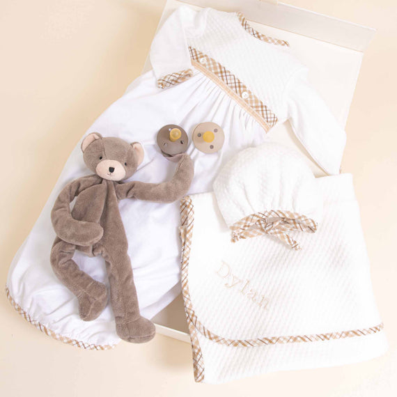 A newborn baby’s Dylan Newborn Gift Set for coming home from the hospital, featuring personalized items including a monogrammed white blanket, a gray teddy bear, tiny booties, and a baby hat, all