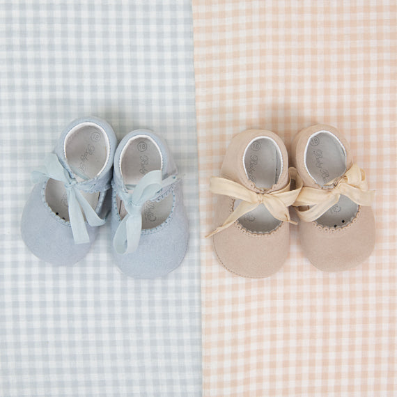 Two pairs of Isla Suede Tie Mary Janes, one blue and one beige, with ribbon laces, arranged symmetrically on a dual-tone checkered background.