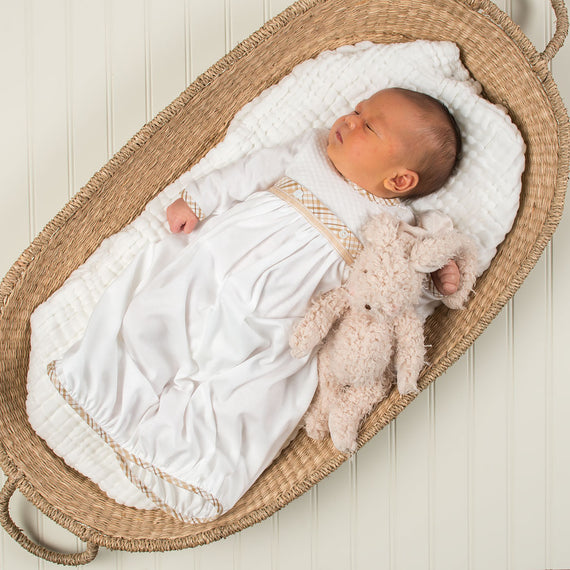 A newborn baby sleeps peacefully in a Dylan Layette, dressed in a boutique outfit. Beside the baby is a soft, plush teddy bear, both resting on a white cushioned liner.