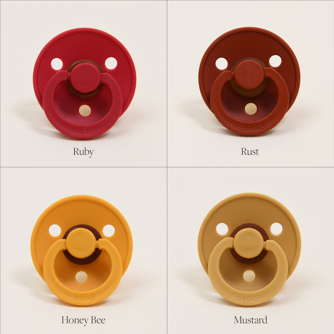 Four colorful Bibs Pacifiers against a white background, displayed in squares. Top left: ruby (red), top right: rust (brown), bottom left: honey bee (yellow), bottom right: