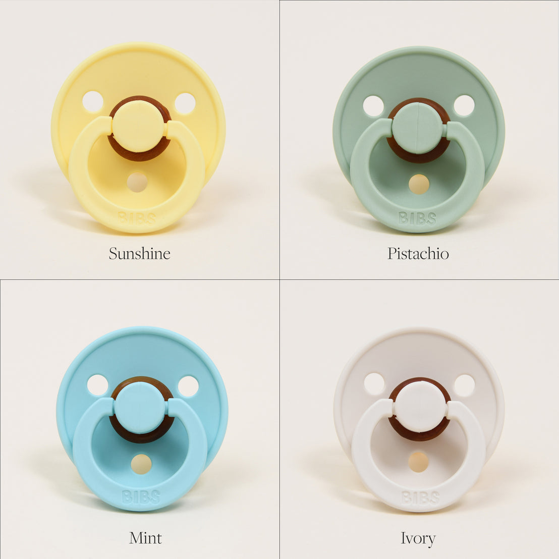 Four Bibs Pacifiers in different colors labeled as sunshine, pistachio, mint, and ivory, displayed against a plain background. Each pacifier has a distinctive round shield and button handle.