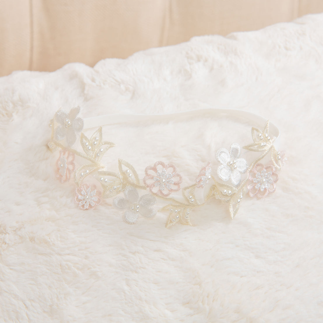 An elegant Jessica Beaded Flower Headband with intricate lace and bead detailing, adding a vintage touch, laid on a soft, white fluffy background.