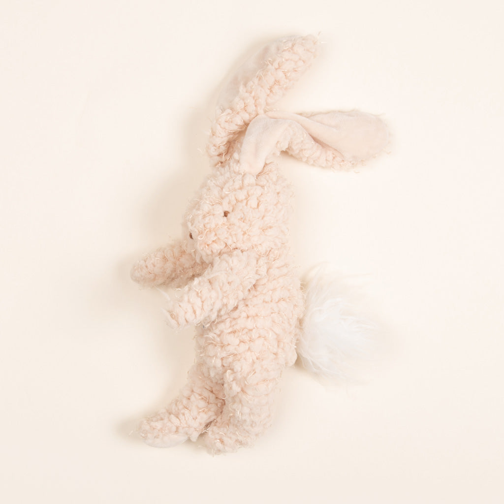 A soft, plush Harey Bunny toy with floppy ears and a fluffy tail, lying on a light beige background. The toy is textured, primarily in a light cream hue.