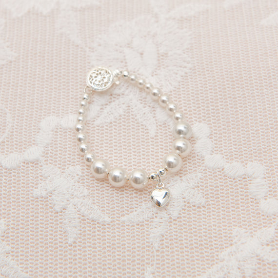 A White Luster Pearl bracelet with an upscale Silver Heart charm, displayed on a delicate pink lace background.