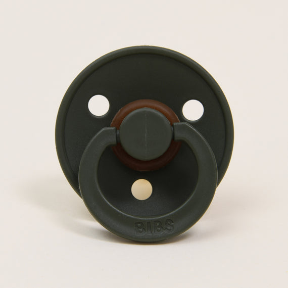 A dark green Bibs Pacifier in Hunter with a brown knob in the center, featuring two ventilation holes and branded with "bibs" at the bottom, displayed against a light beige background.