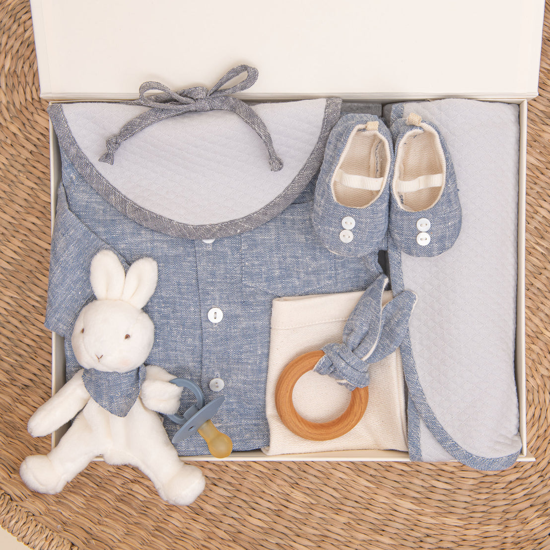 Photo of the indigo colored Silas Gift Set in a Gift Box. Included in the box is the shirt, pants, booties, bib, teether, bunny, pacifier, and personalized blanket.
