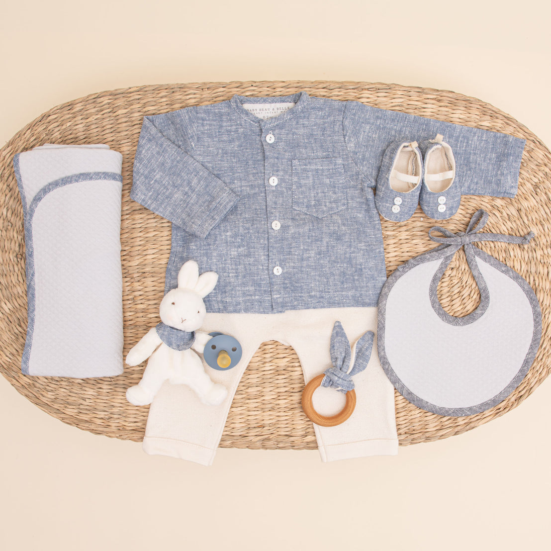 Flat lay photo of the indigo colored Silas Gift Set. Included in the photo is the shirt, pants, booties, bib, teether, bunny, pacifier, and personalized blanket.