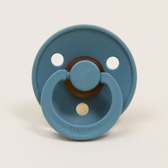 A teal-colored Bibs Pacifier 2 Pack | Island Sea with a round shield, two ventilation holes, and a handle, branded "bibs" on a neutral background.