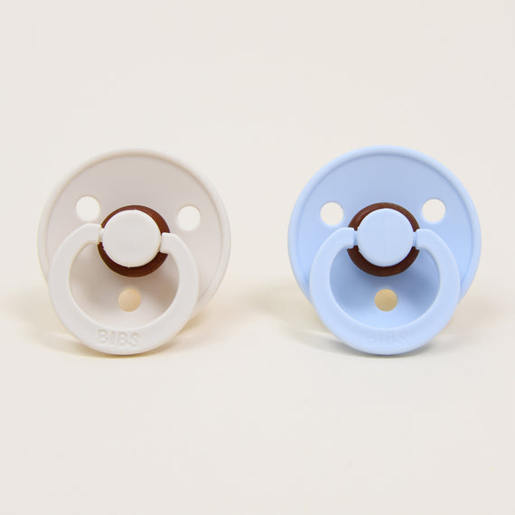 Photo of two pacifiers in two different colors: ivory and baby blue