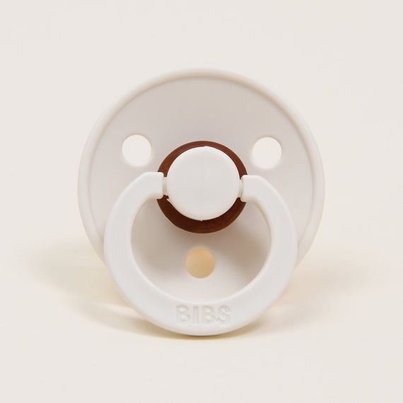 A Bibs Pacifier in Ivory with a brown center button and handle, set against a plain beige background.