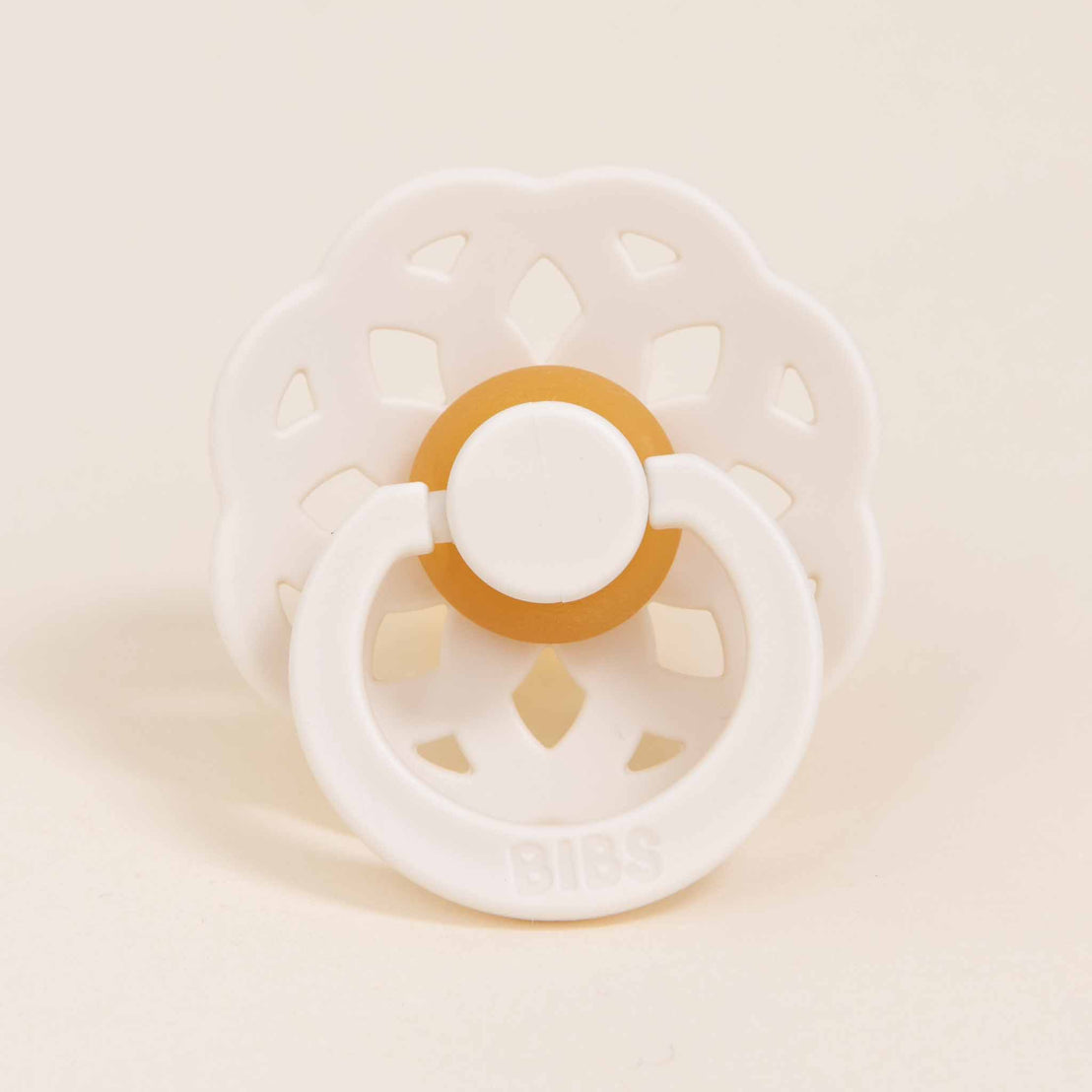 The Ava pacifier in ivory with a flower-shaped silicone pacifier and button center labeled "Bibs" on a beige background.