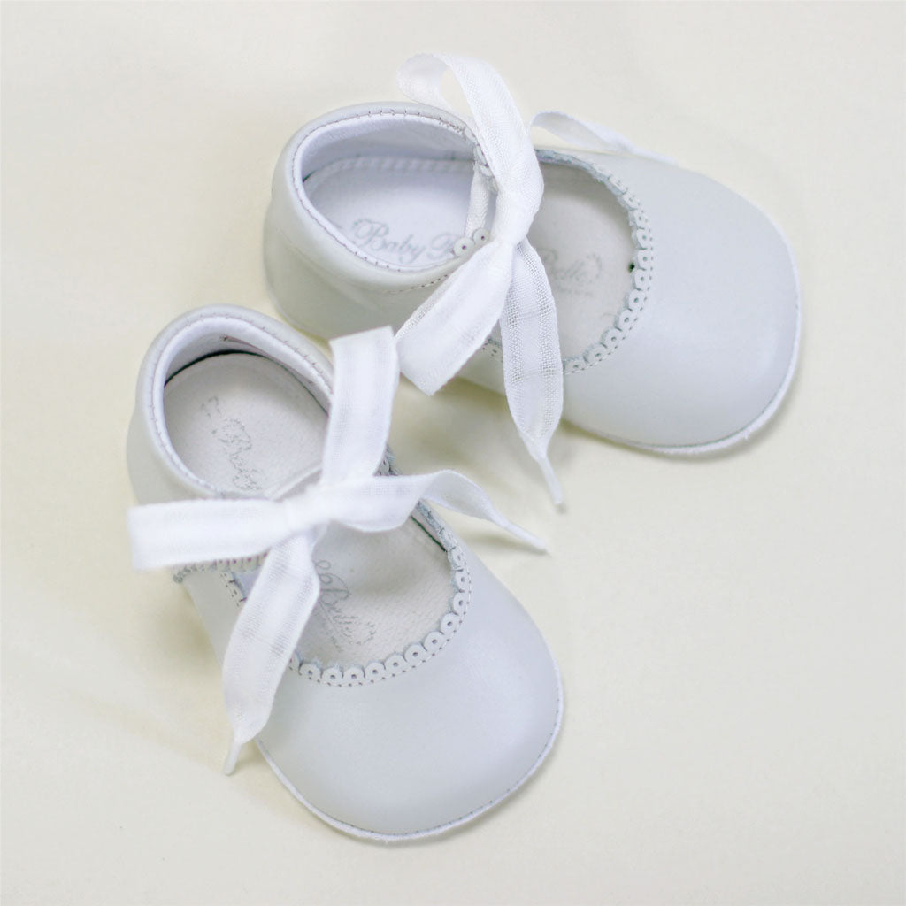 A pair of Ivory Tie Mary Janes with ribbon ties and delicate lace detailing, displayed against a soft beige background.