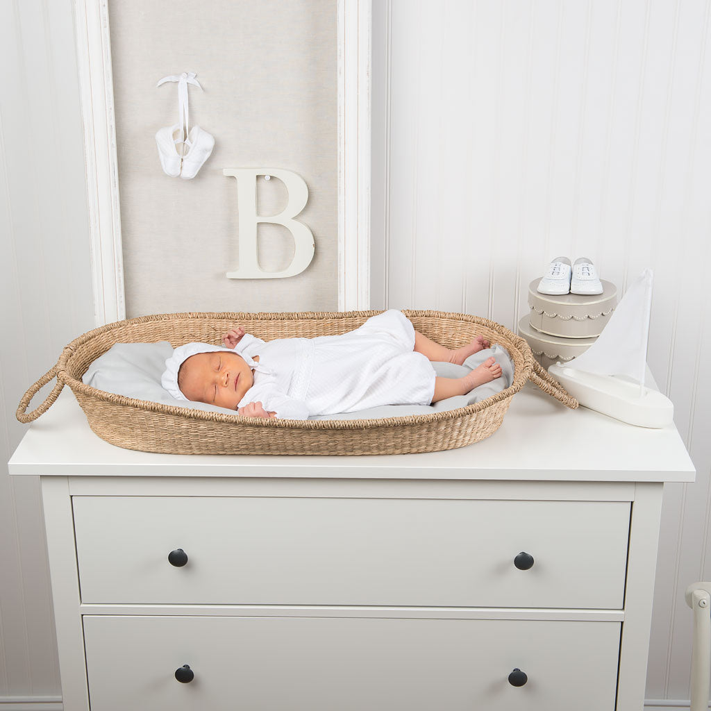 A newborn baby sleeps in a cradle. He is wearing the Elijah Newborn Romper made from a plush white quilted cotton, featuring white Venice lace at the bodice and white linen trim at the cuffs and neck