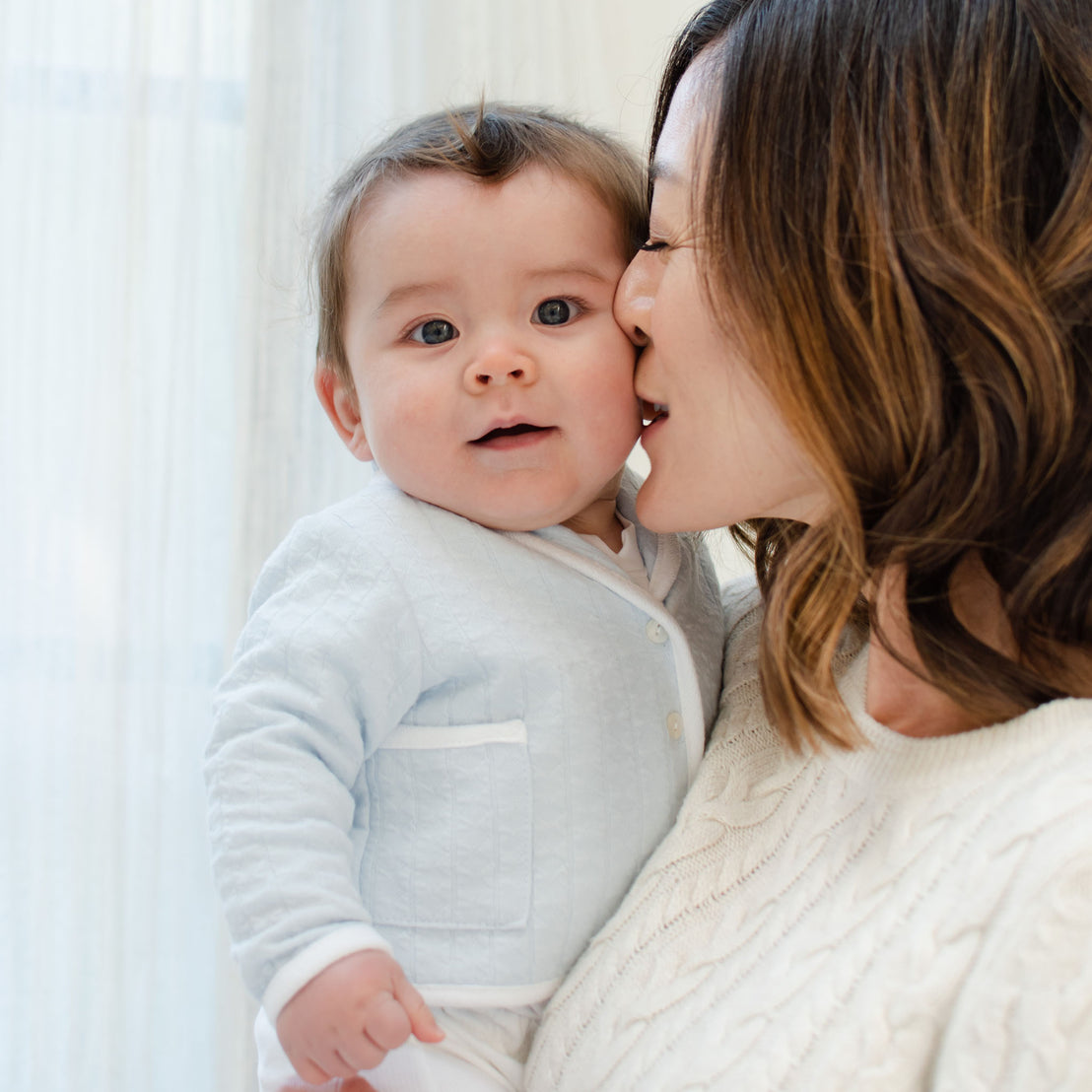 Baby boy with his mother and wearing the Logan 3-Piece Suit, including the jacket, pants and onesie. Jacket made from blue textured cotton with a white French terry cotton trim.
