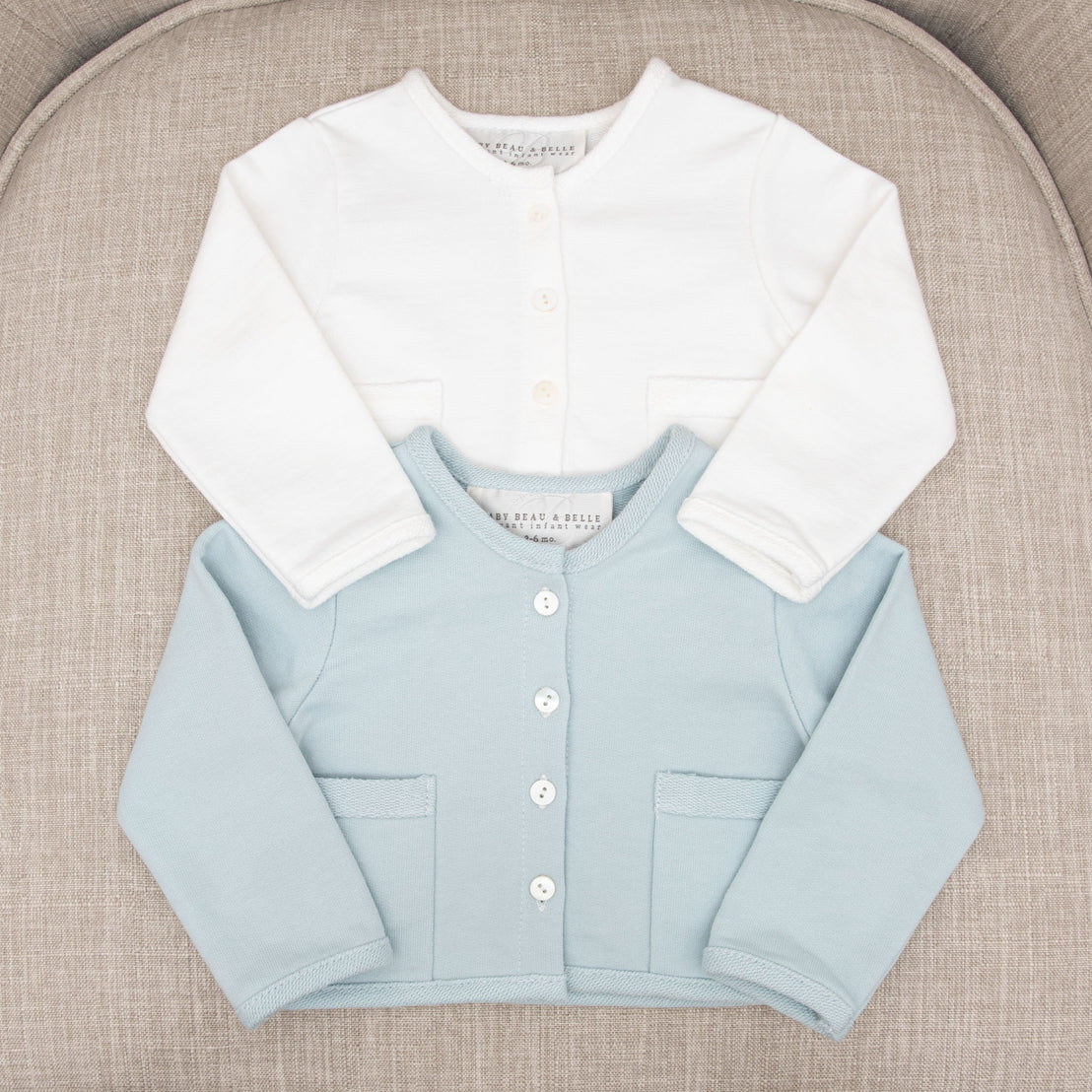 Two Ian French Terry Jackets laid flat on a gray textured chair; the top one is white and the bottom one is light blue, both with front buttons from a boutique.