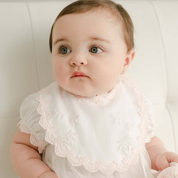 A baby with large eyes and a round face wearing a Joli Bib, sitting and looking slightly upward with a curious expression.