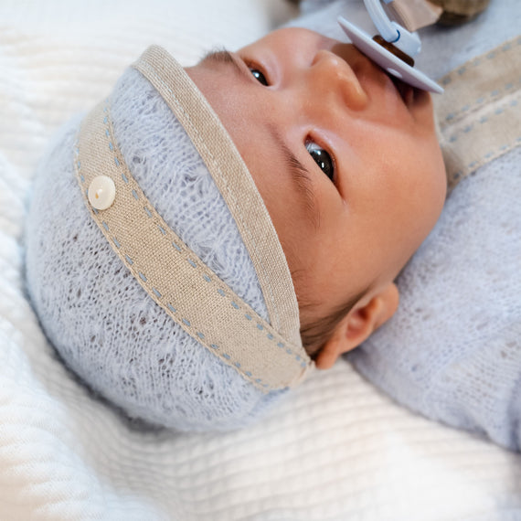 Close-up of a newborn baby with a pacifier, wearing an Austin Hat and a cozy jumper, lying down and looking away from the camera.