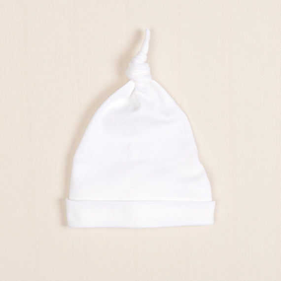 A white Dylan Knot Cap baby hat with a knotted top on a light beige background.