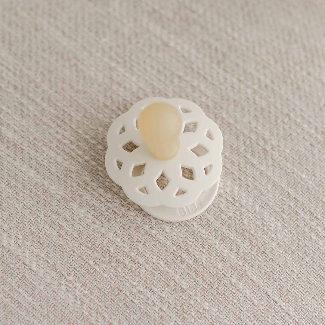 A vintage-inspired, white, lattice-designed  on a textured beige surface, with its central knob in a muted orange shade.