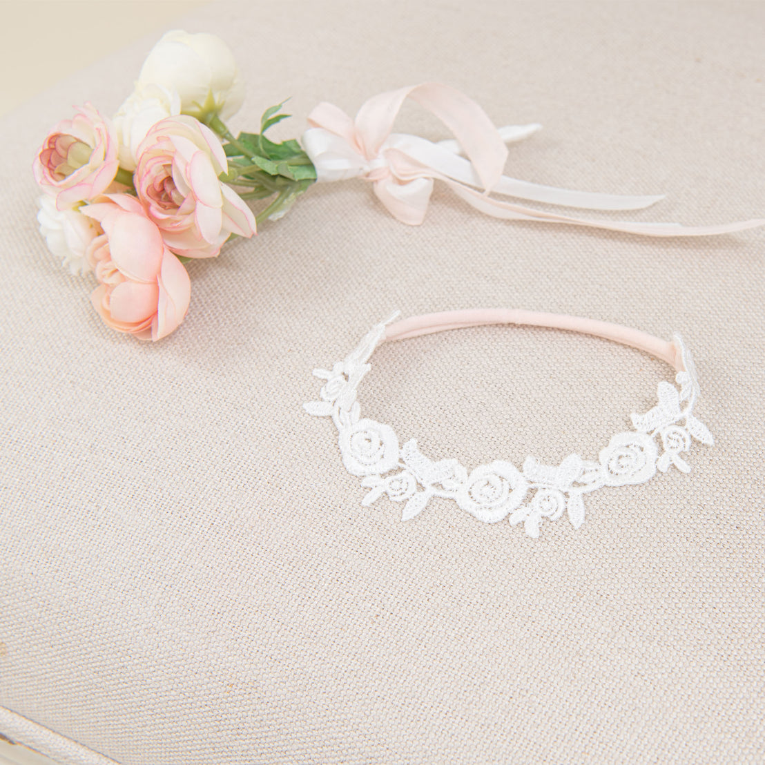 A delicate Rose Lace Headband beside a bouquet of soft pink and white flowers tied with a light pink ribbon, all set against a textured beige background.