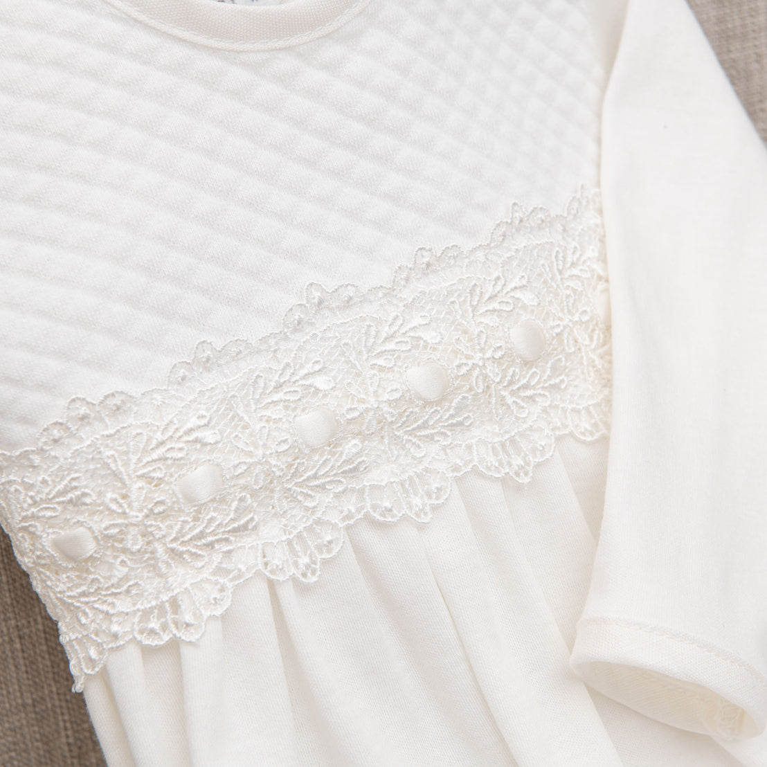 Close-up of a white lace detail on Madeline Newborn Gown, accenting the neckline and sleeves, against a soft grey background.